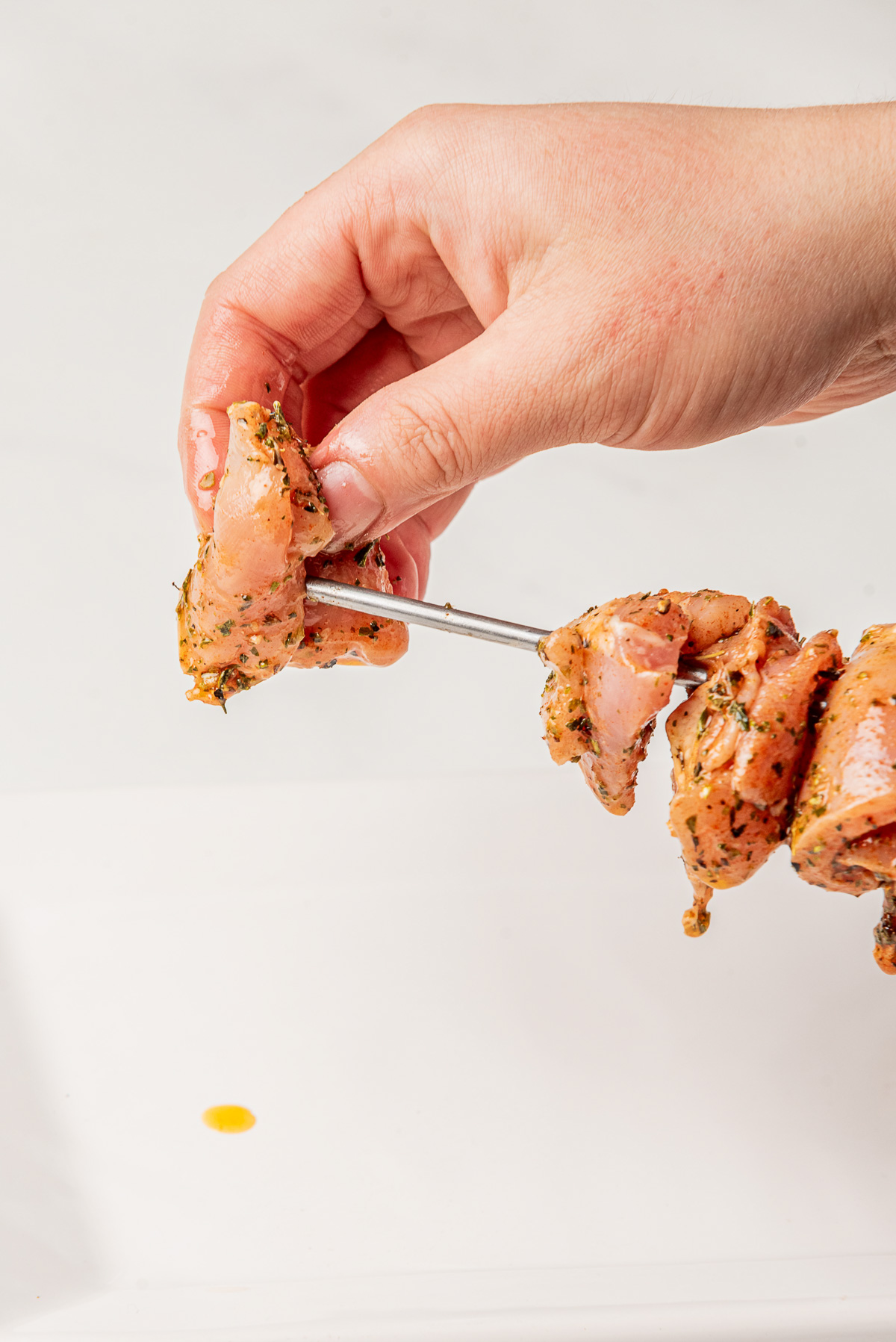 Chicken thighs being added to a metal skewer.