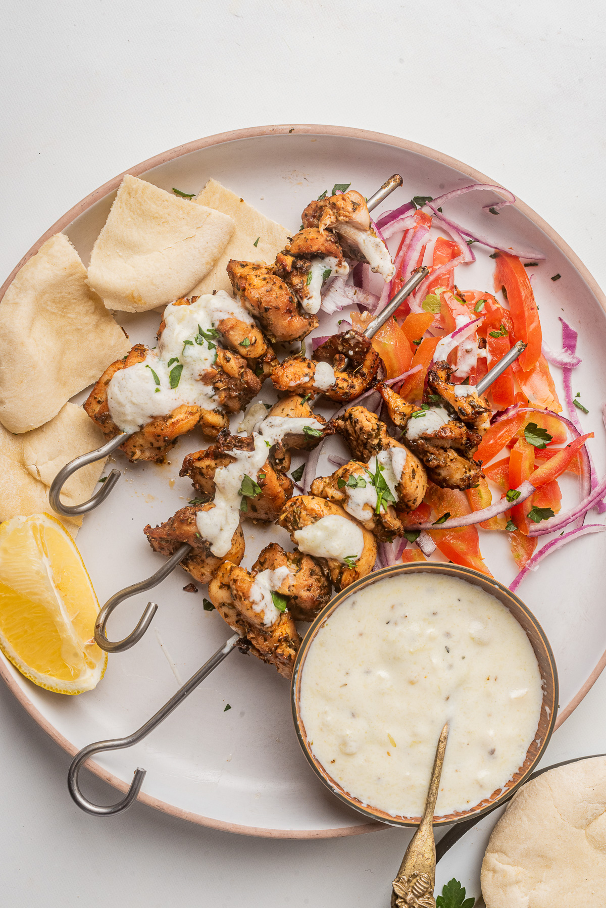Overhead view of Greek chicken kebabs on a white plate with tzatziki and other sides.