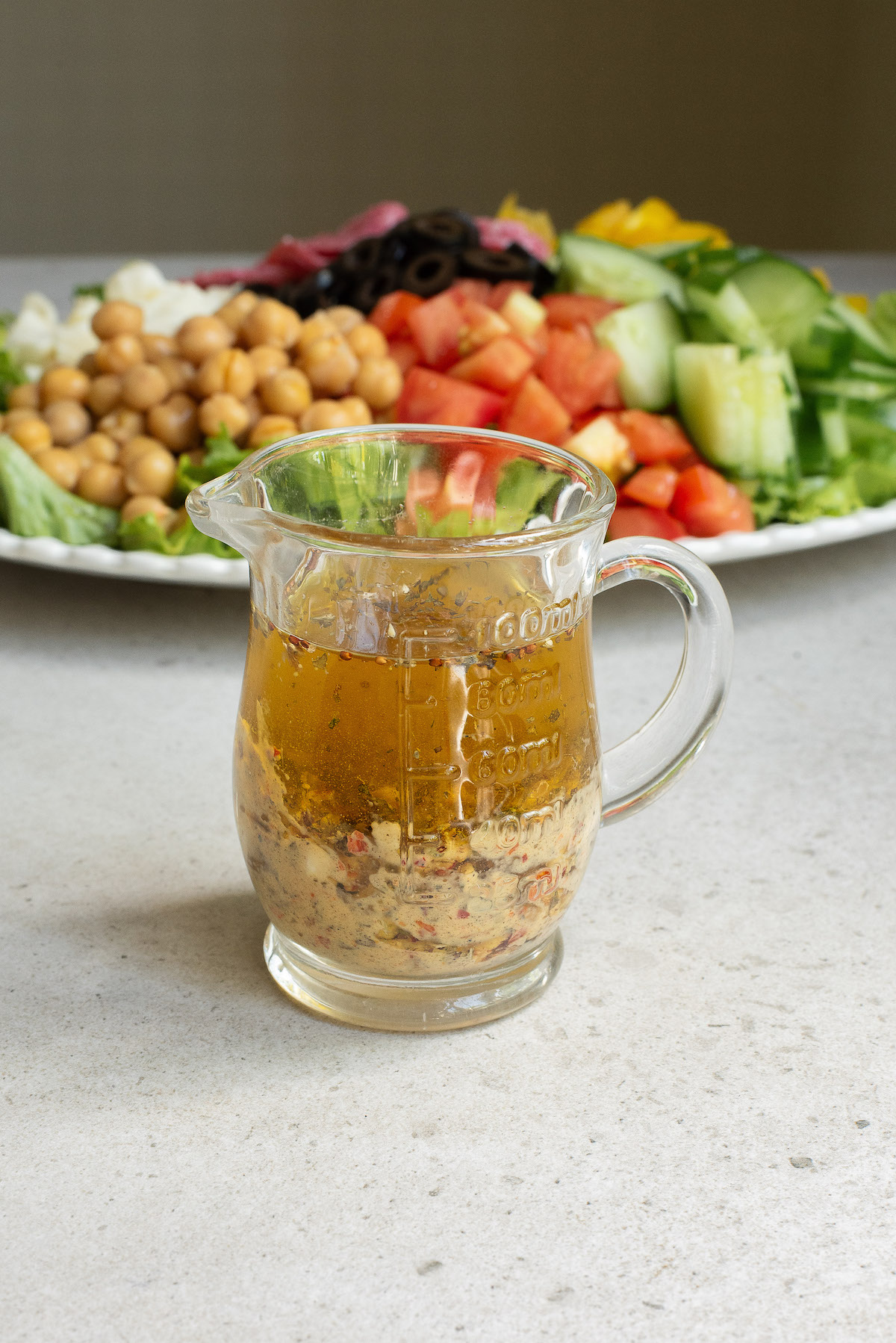 a glass pitcher of salad dressing set in front of the chopped salad