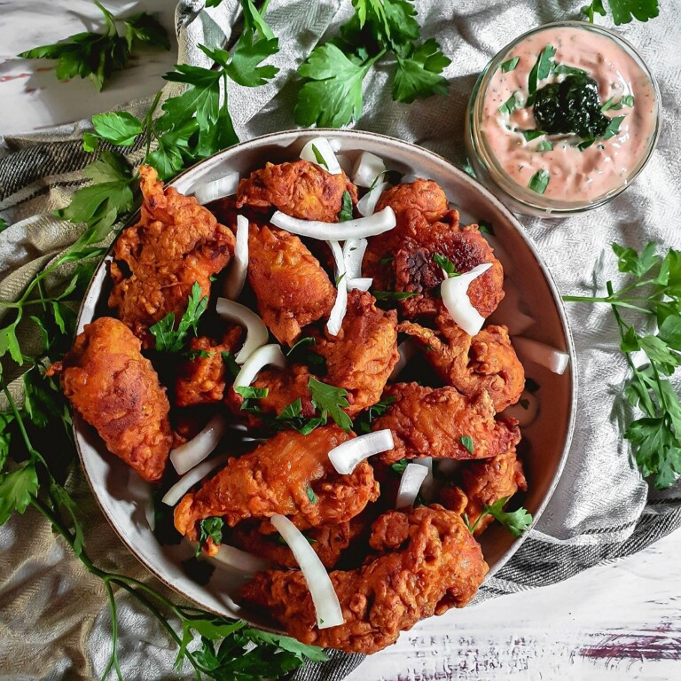 Chicken Pakora in a white bowl with onion on top.