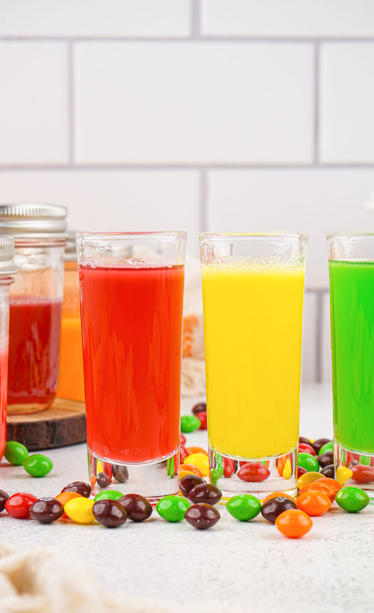 three glasses of candy-infused vodka on a counter with Skittles scattered in front