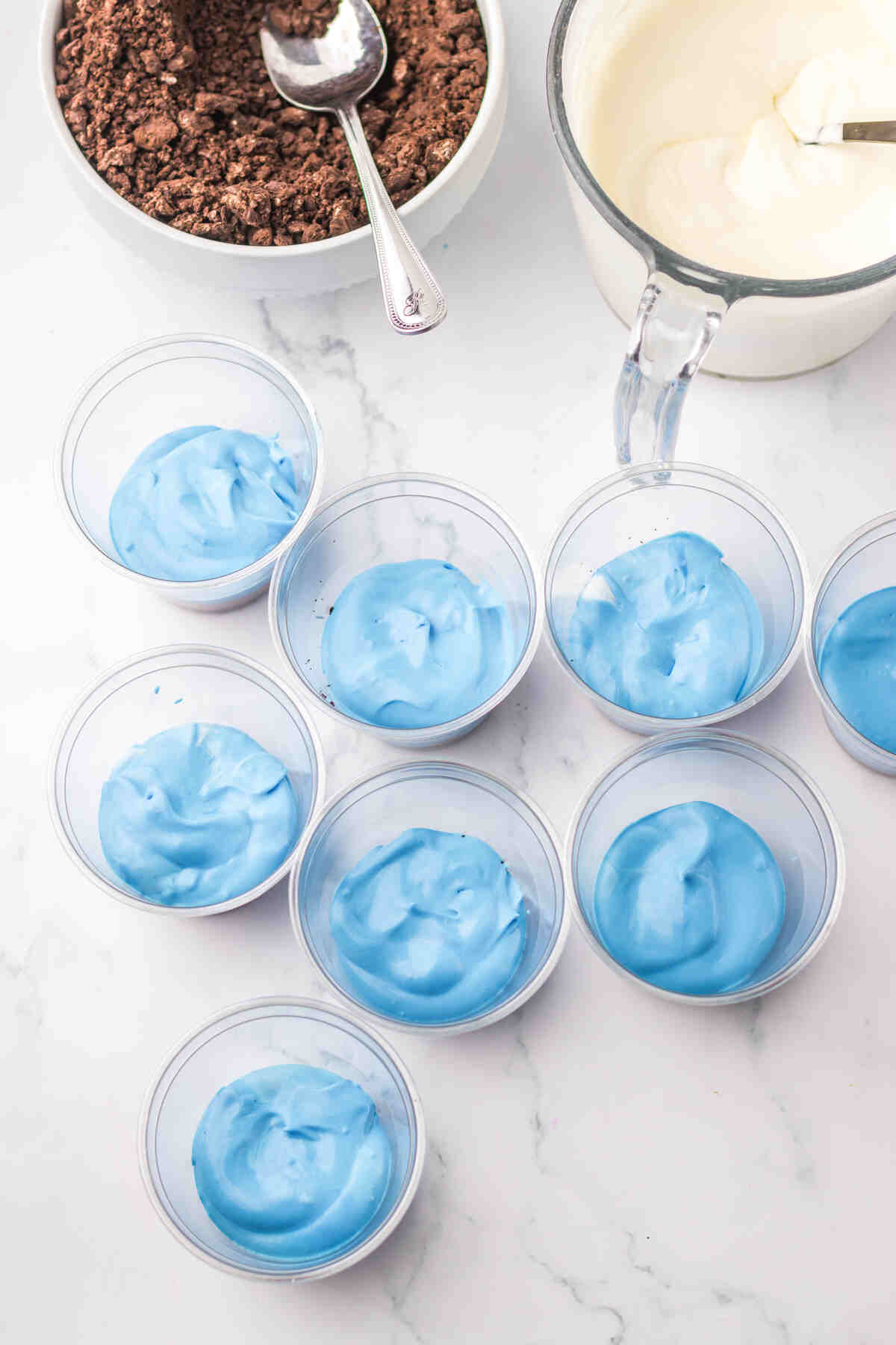blue pudding being layered on top of cookie crumbs inside individual serving dishes.
