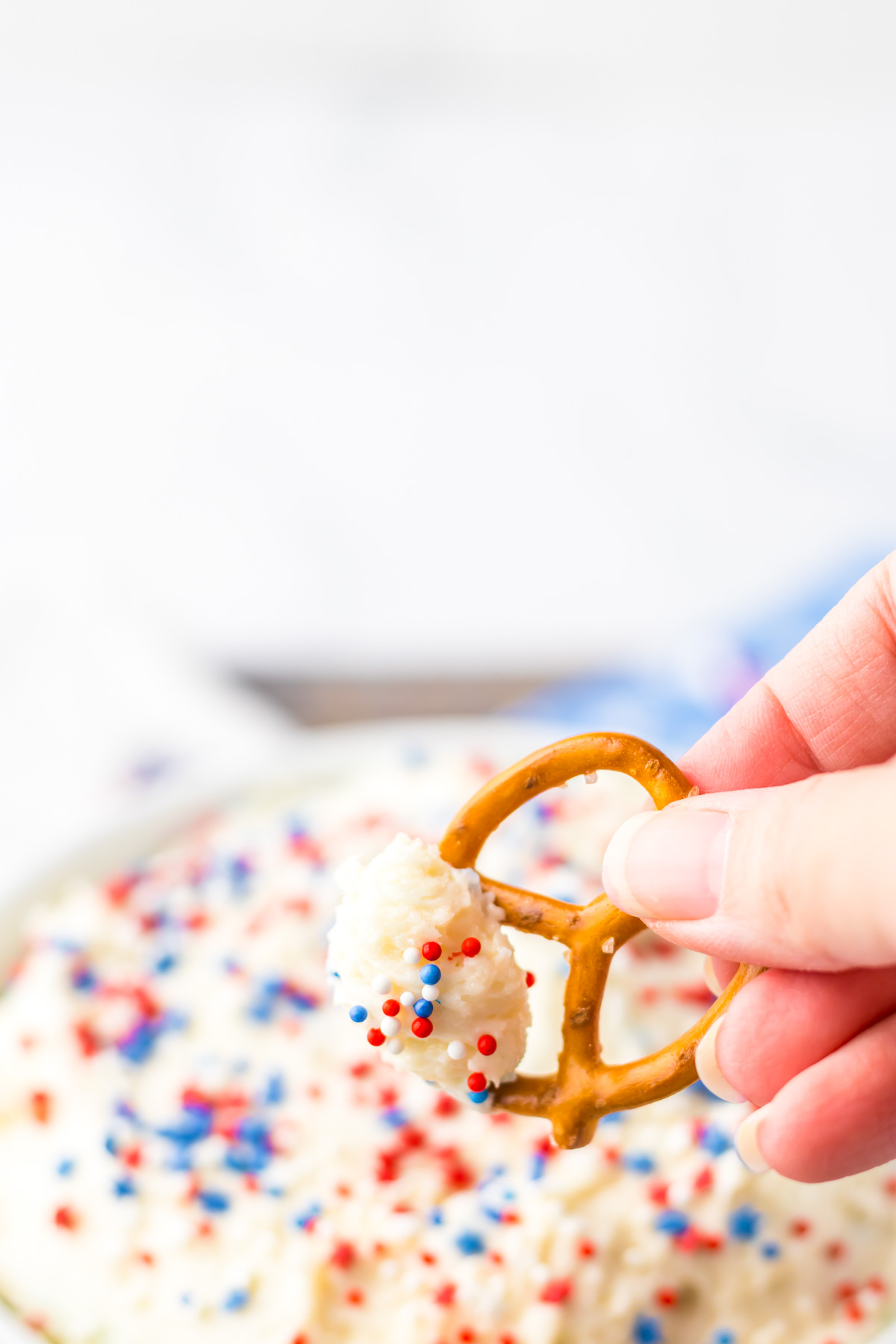 a hand dipping one pretzel into the cake batter dip.