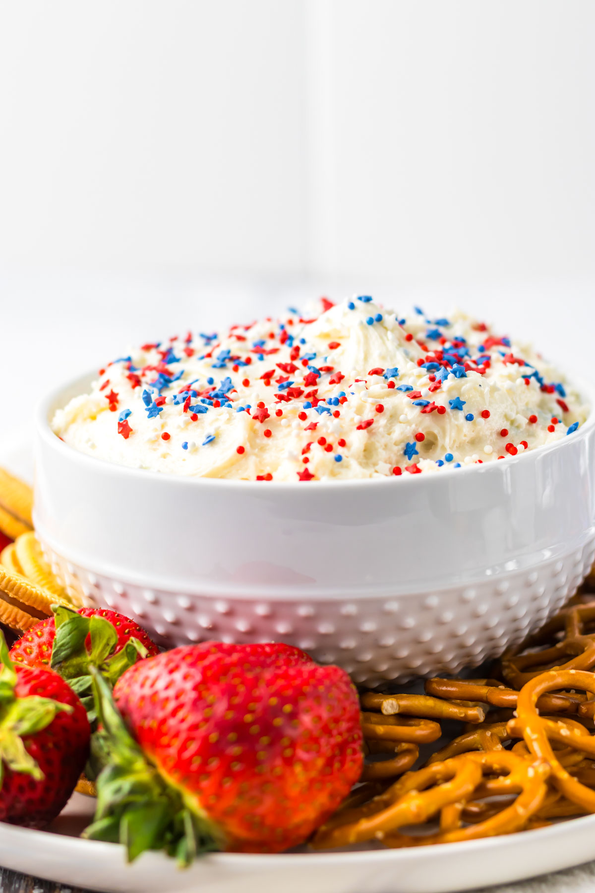 the finished funfetti dip recipe in a bowl on top of a serving platter with strawberries and preztel dippers.