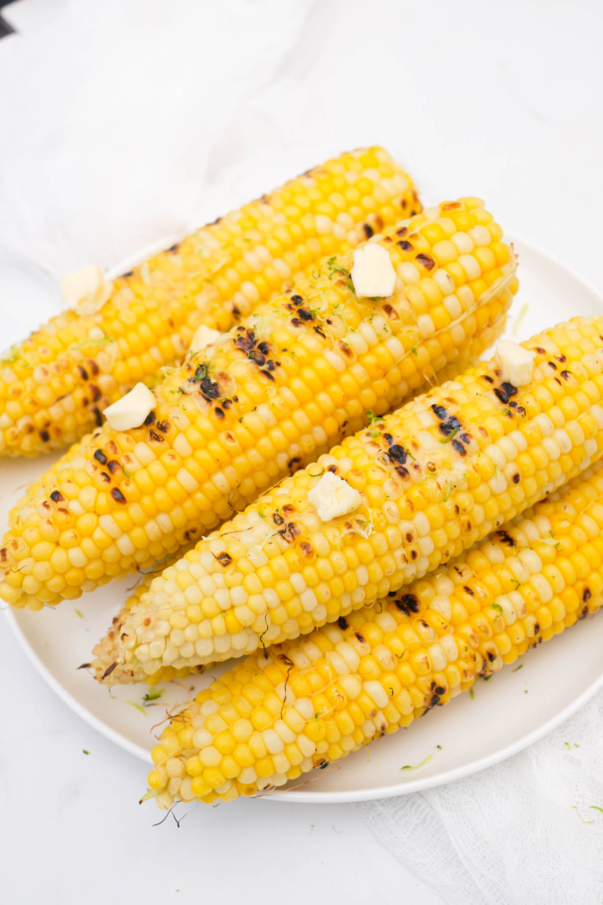 5 pieces of grilled corn topped with butter and stacked on a white plate
