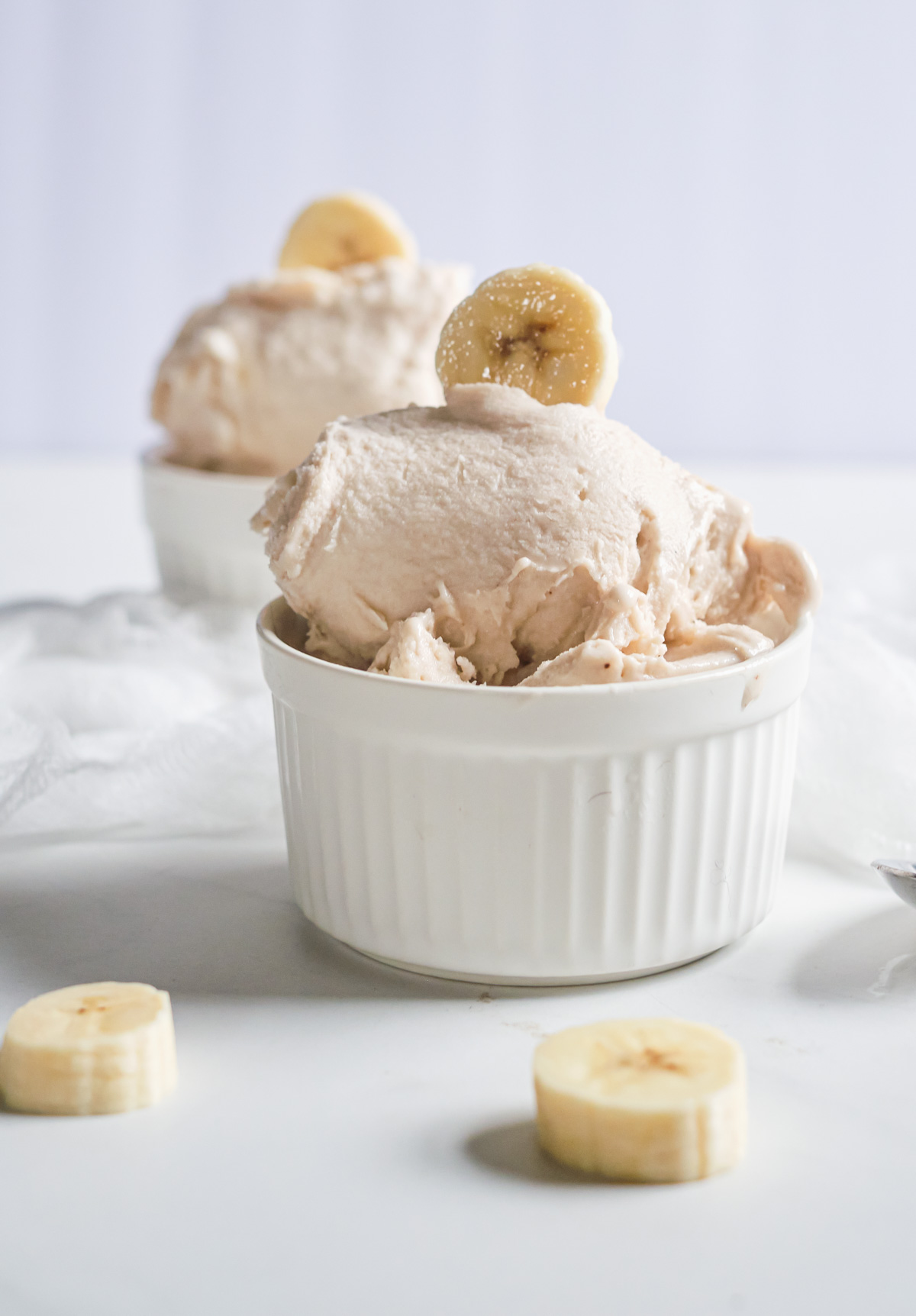 a scoop of banana ice cream in a white dish and topped with fresh banana slices