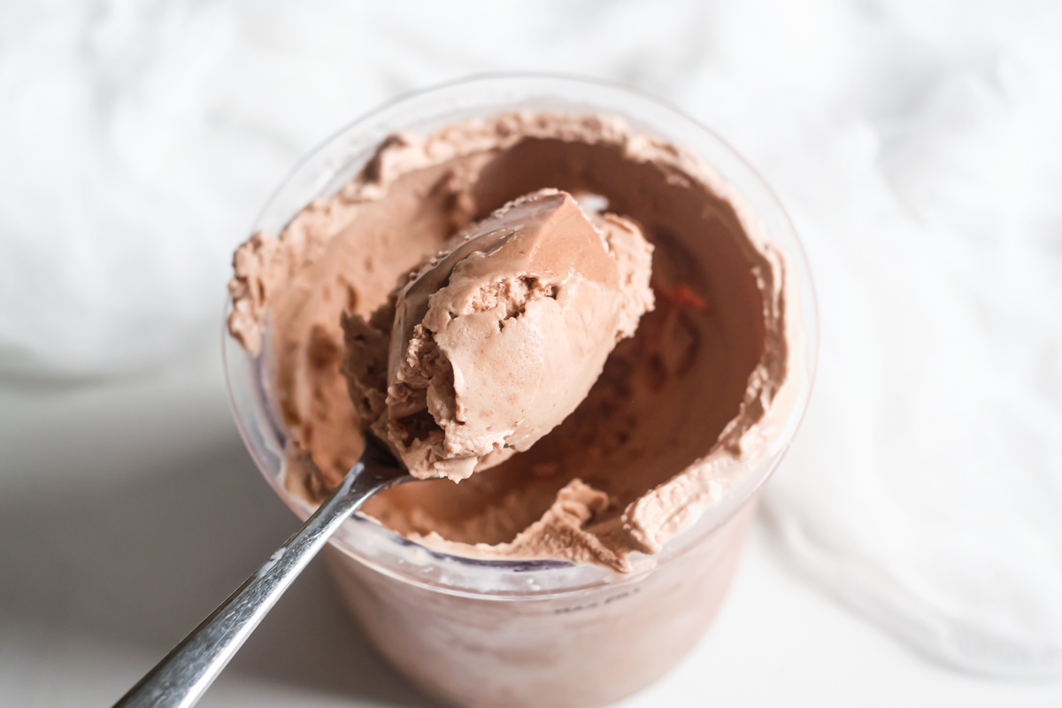 a spoon removing some of the homemade chocolate ice cream from a pint container.
