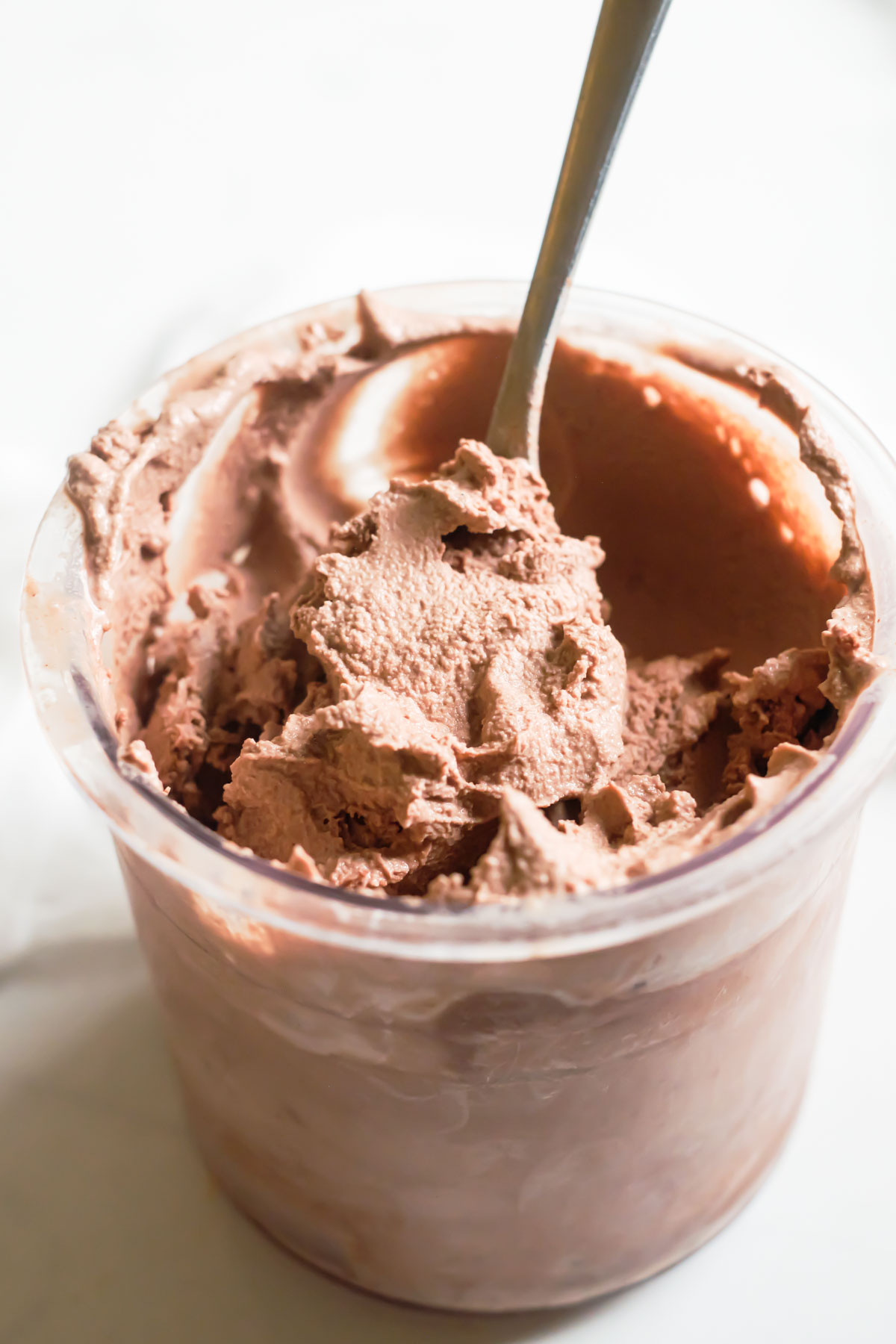 a spoon removing a portion of the finished Ninja Creami Chocolate ice cream from a glass container