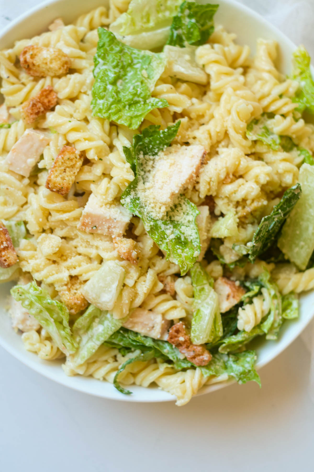 top down view of the caesar pasta salad with chicken served in a white bowl.