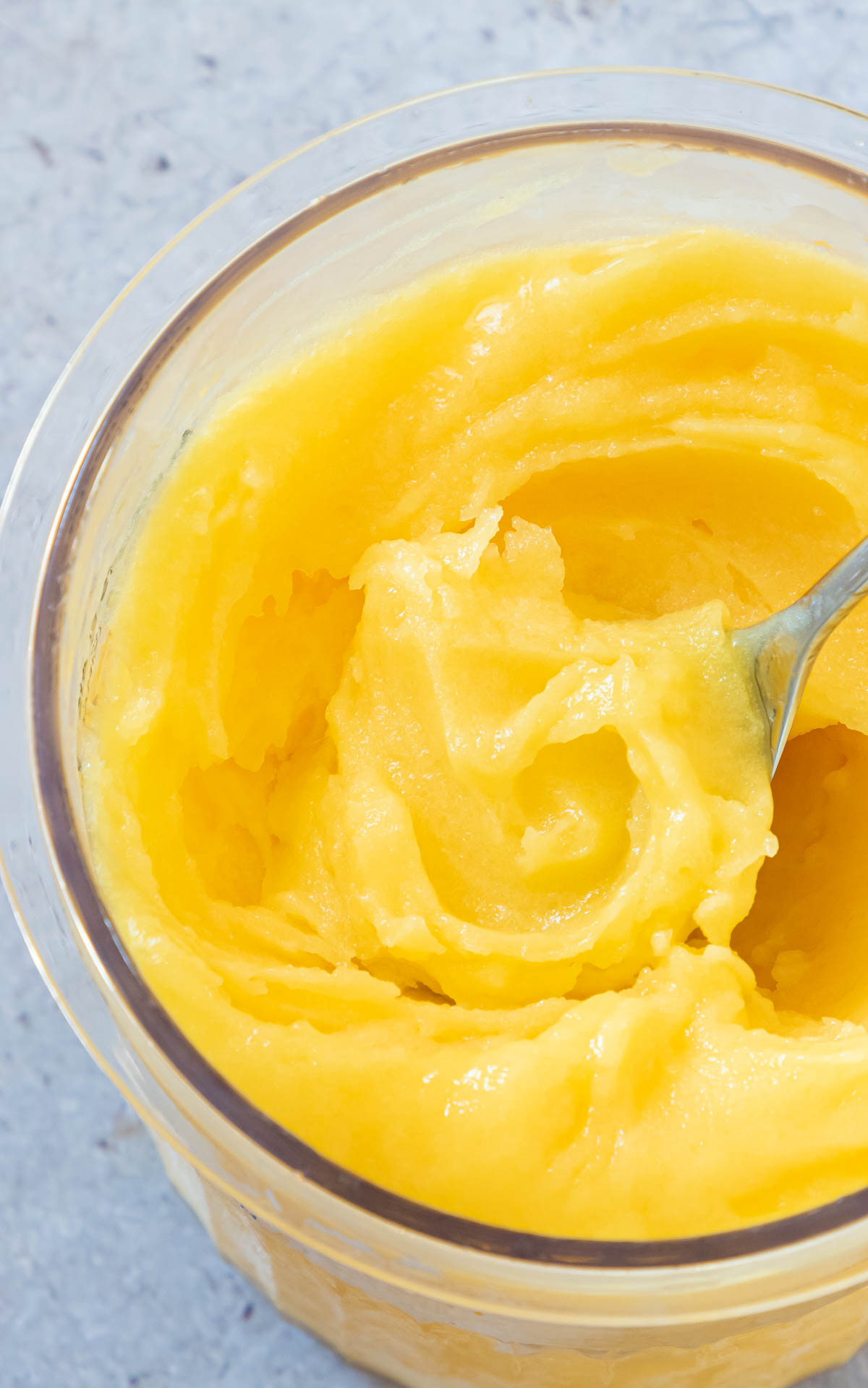 close up view of a spoon scooping some of the mango sorbet out of a pint container.
