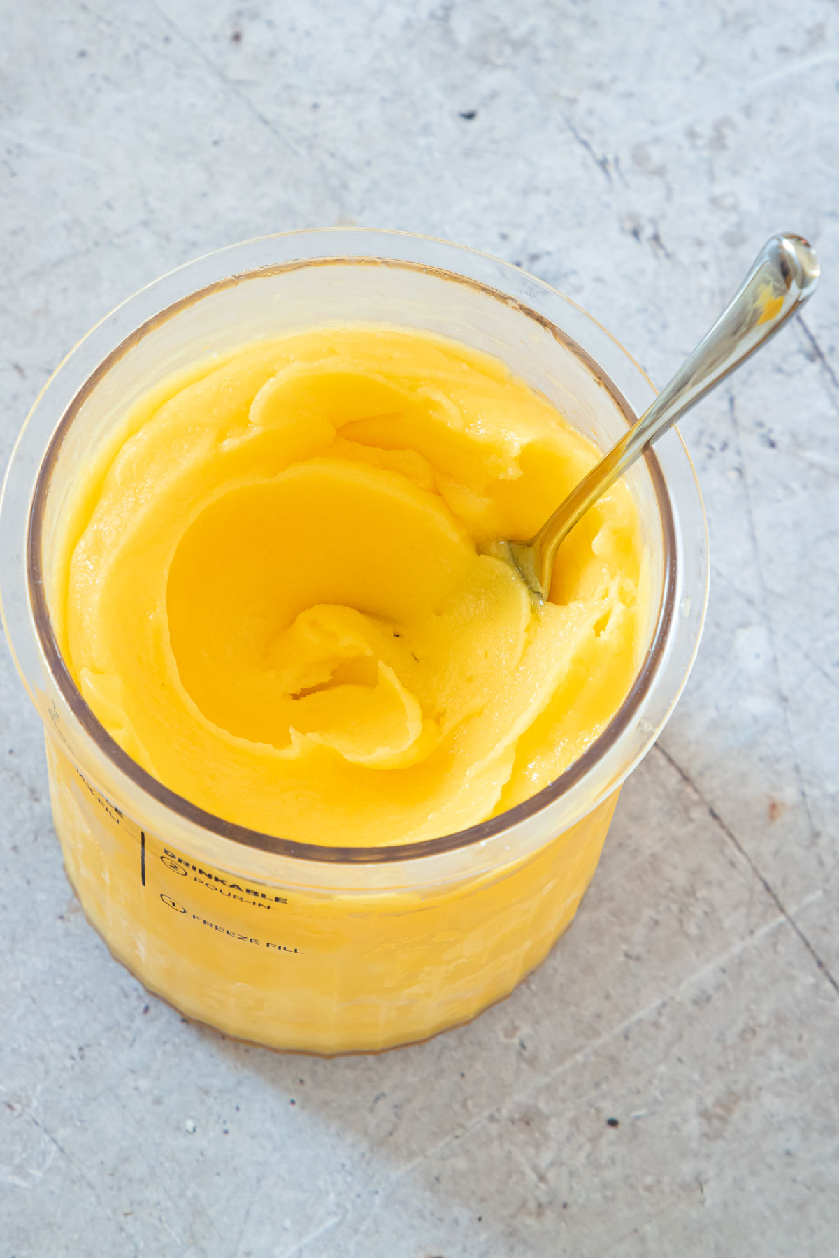 the completed mango sorbet in a pint container with a serving spoon.