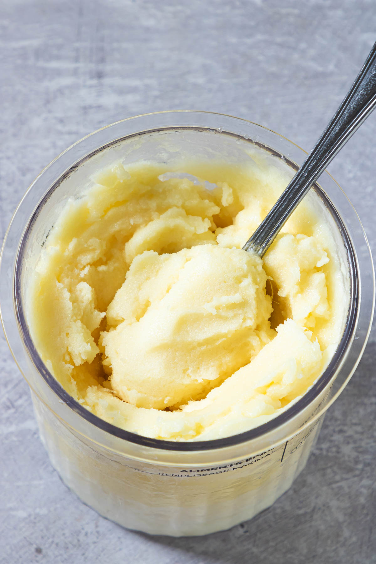 a spoon removing a portion of the Ninja Creami pineapple sorbet from a pint container.