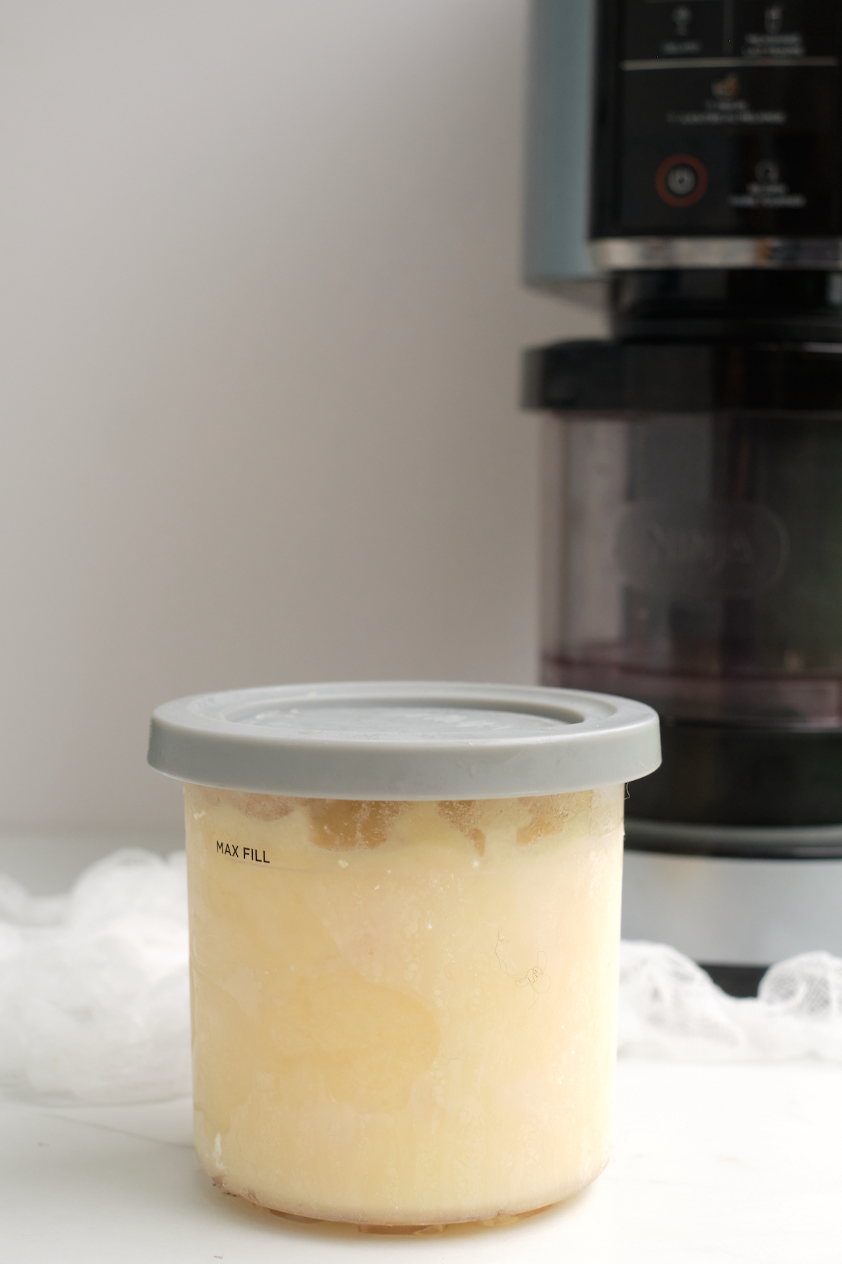 a pint container of pineapple sorbet placed in front of the Ninja Creami machine.