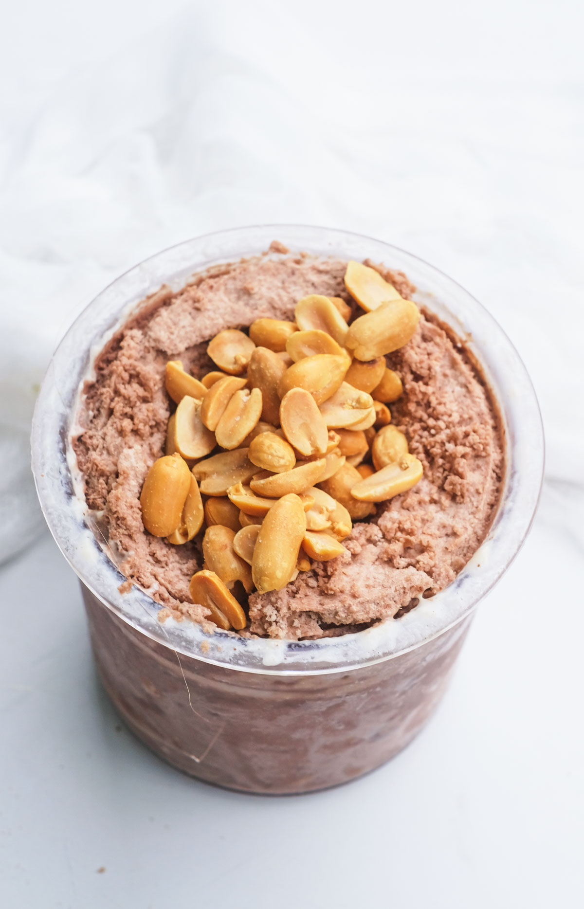 A pint of chocolate peanut butter protein ice cream topped with chopped peanuts.