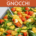 A spoon scooping gnocchi and vegetables off of a sheet pan