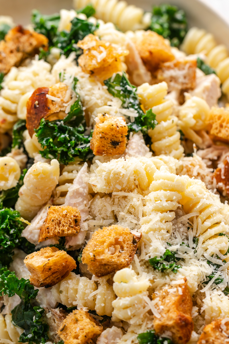 Close-up shot showing the texture of rotini pasta, crisp kale, golden croutons, and Parmesan.