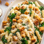 Creamy Chicken Caesar Pasta Salad arranged on a serving platter with kale, Parmesan, and homemade croutons.