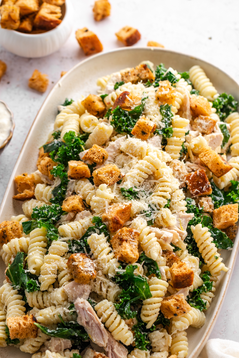 Creamy Chicken Caesar Pasta Salad arranged on a serving platter with kale, Parmesan, and homemade croutons.