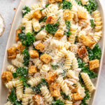 Large serving platter filled with a creamy pasta salad topped with crunchy croutons, kale, and shredded chicken.