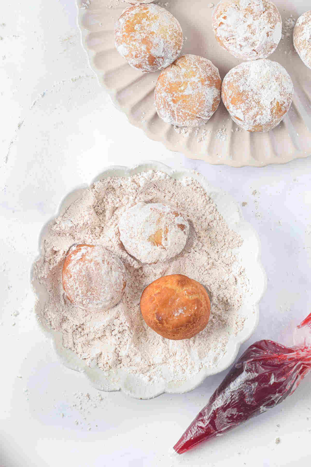 the donuts being coated in cinnamon sugar next to a piping bag filled with jam.