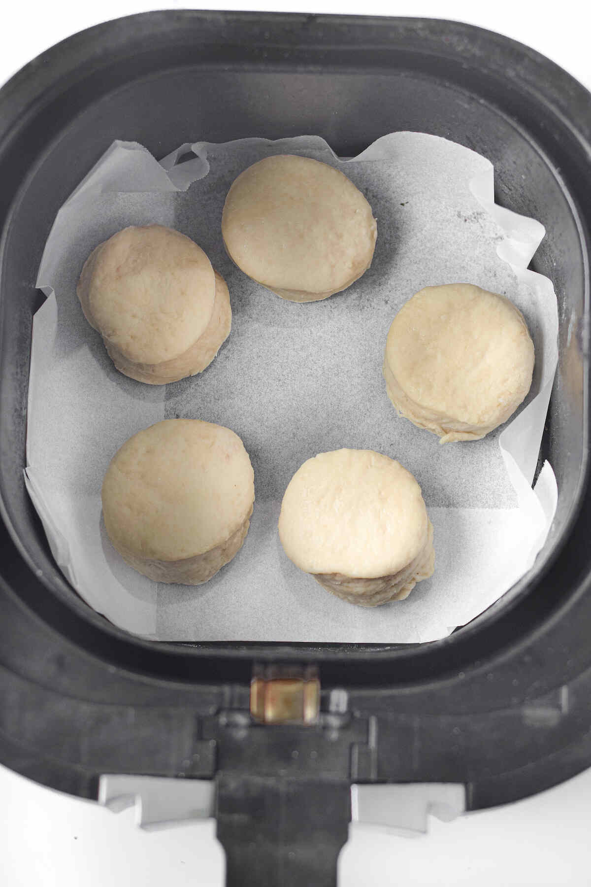 the uncooked donuts inside the air fryer basket.