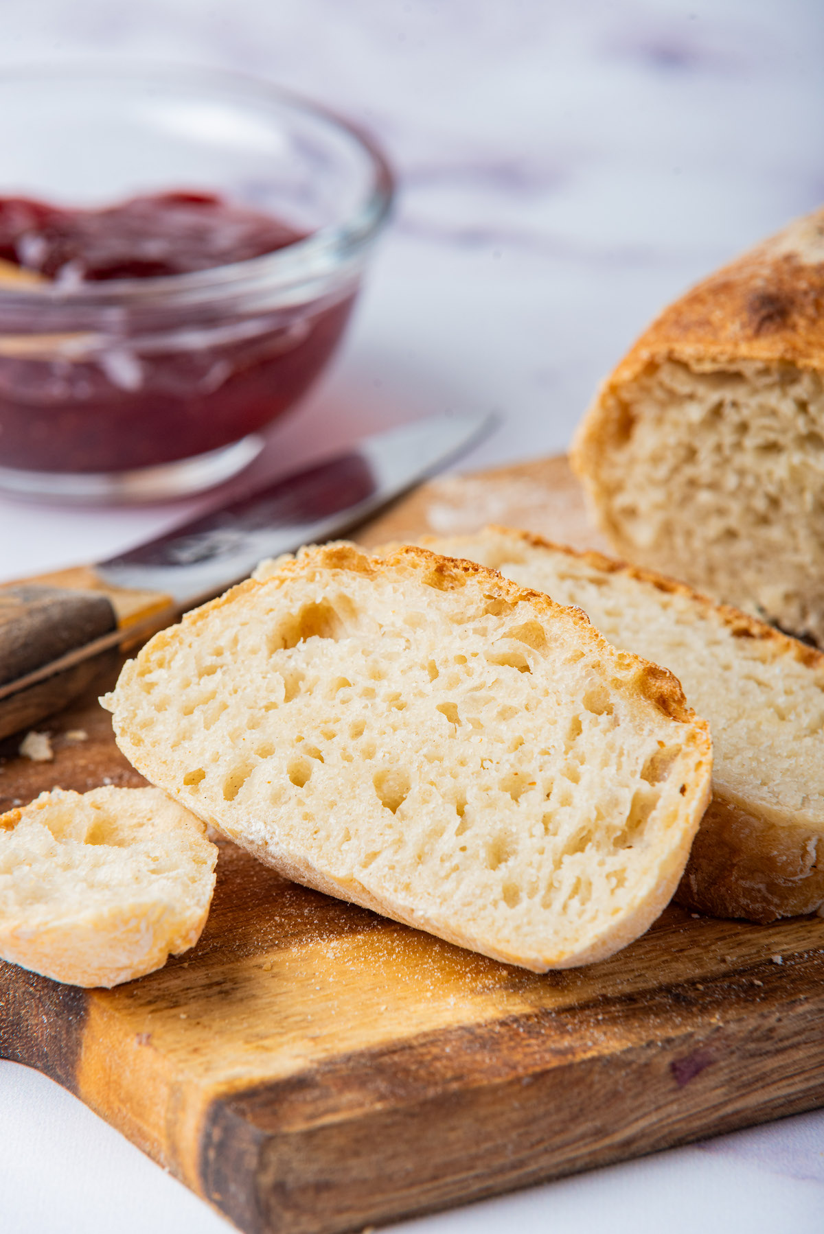 the sliced load of bread on a wooden serving board with a pot of jam and knife.