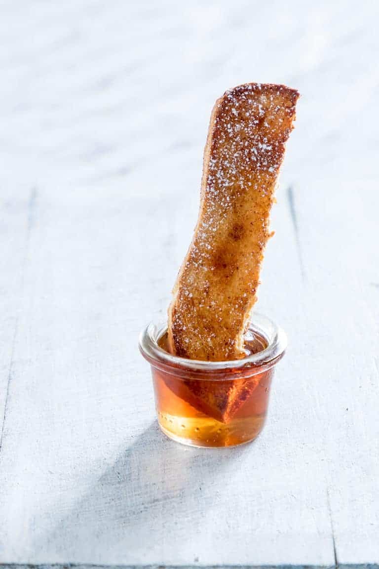 One Air Fryer French Toast Stick dipped into a glass cup filled with syrup