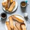 two plates of Air Fryer French Toast Sticks served with syrup and powdered sugar