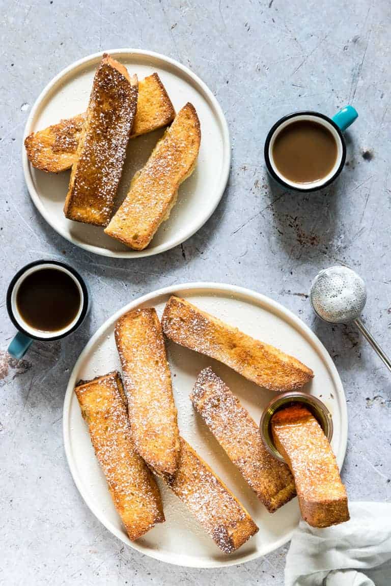 two plates of Air Fryer French Toast Sticks served with syrup and powdered sugar
