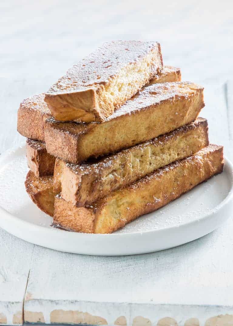 Air Fryer French Toast Sticks stacked onto a white plate.