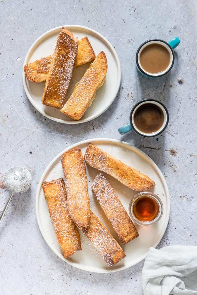 two plates of Air Fryer French Toast Sticks with cups containing syrup, honey and jam