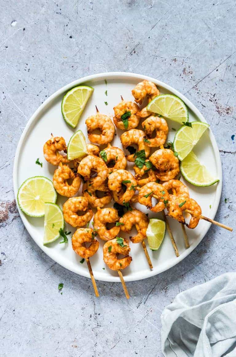 air fryer shrimp skewers on a white plate garnished with chopped cilantro and lime wedges