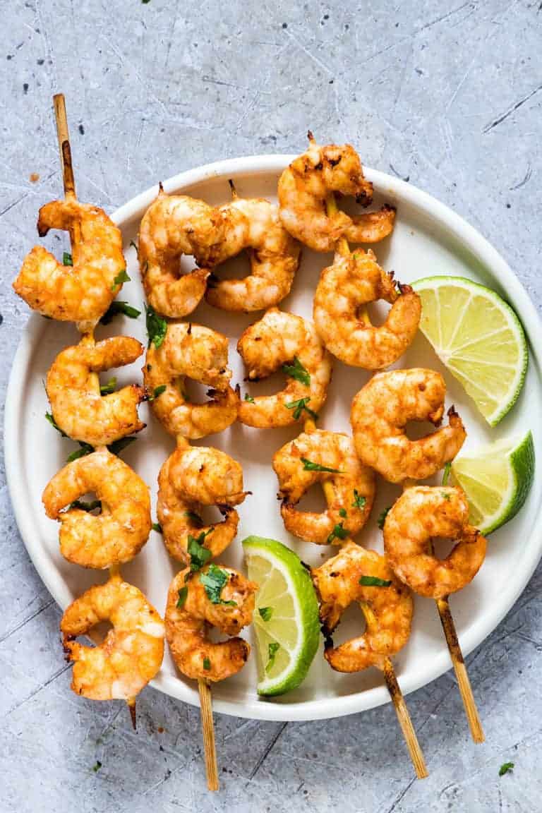 Air Fryer Shrimp Skewers on a while plate an garnished with chopped cilantro and lime wedges