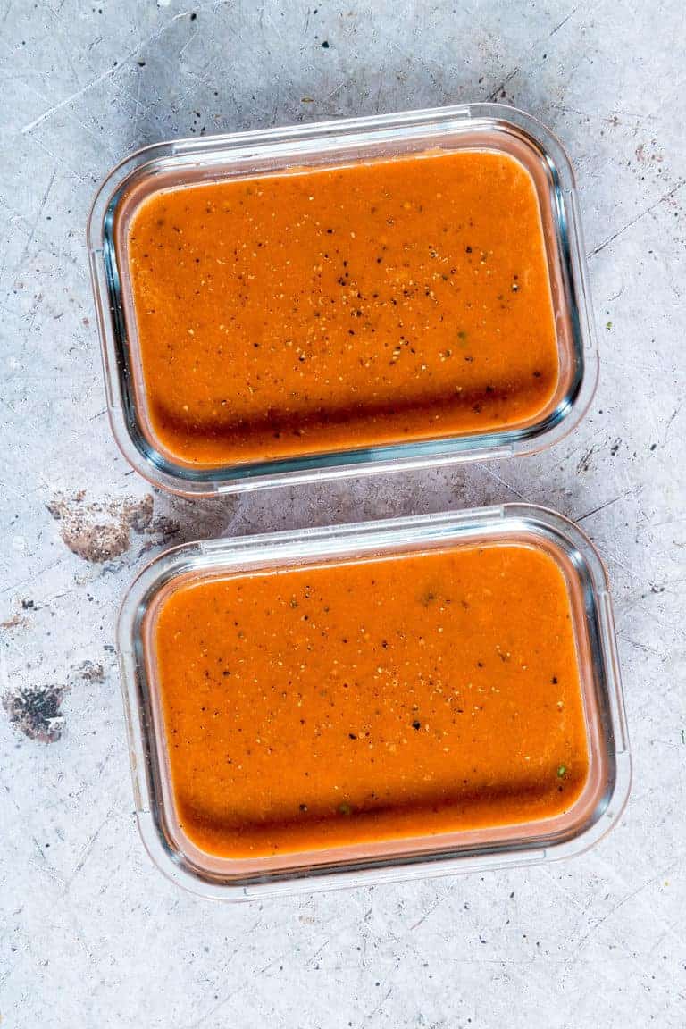two portions of Creamy Tomato Soup in glass meal prep containers ready to be stored in the freezer