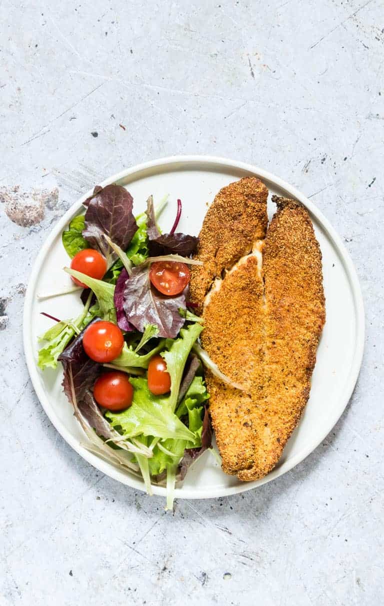 one air fryer fish fillet served with a green salad on a white dinner plate