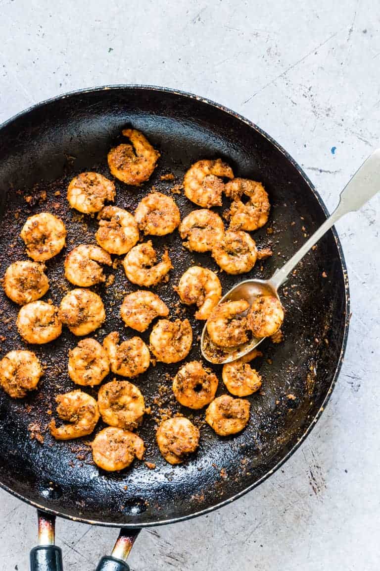 Close up of cooked shrimp in skillet with a spoon scooping out a serving of this Cajun Shrimp Recipe 