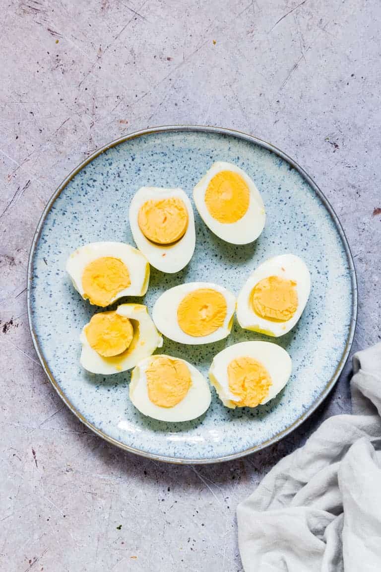 cooked air fryer hard boiled eggs cut in half and served on a blue ceramic plate with a white cloth napkin