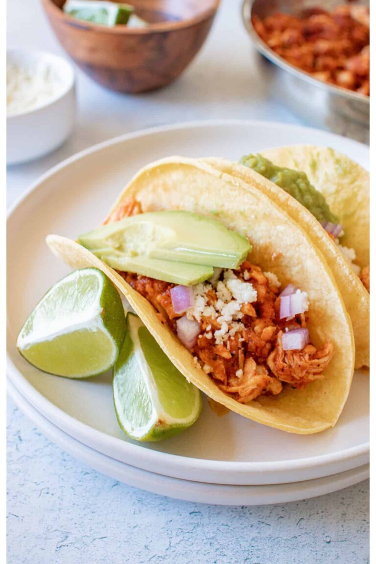 Chicken tinga tacos on a white plate with limes.