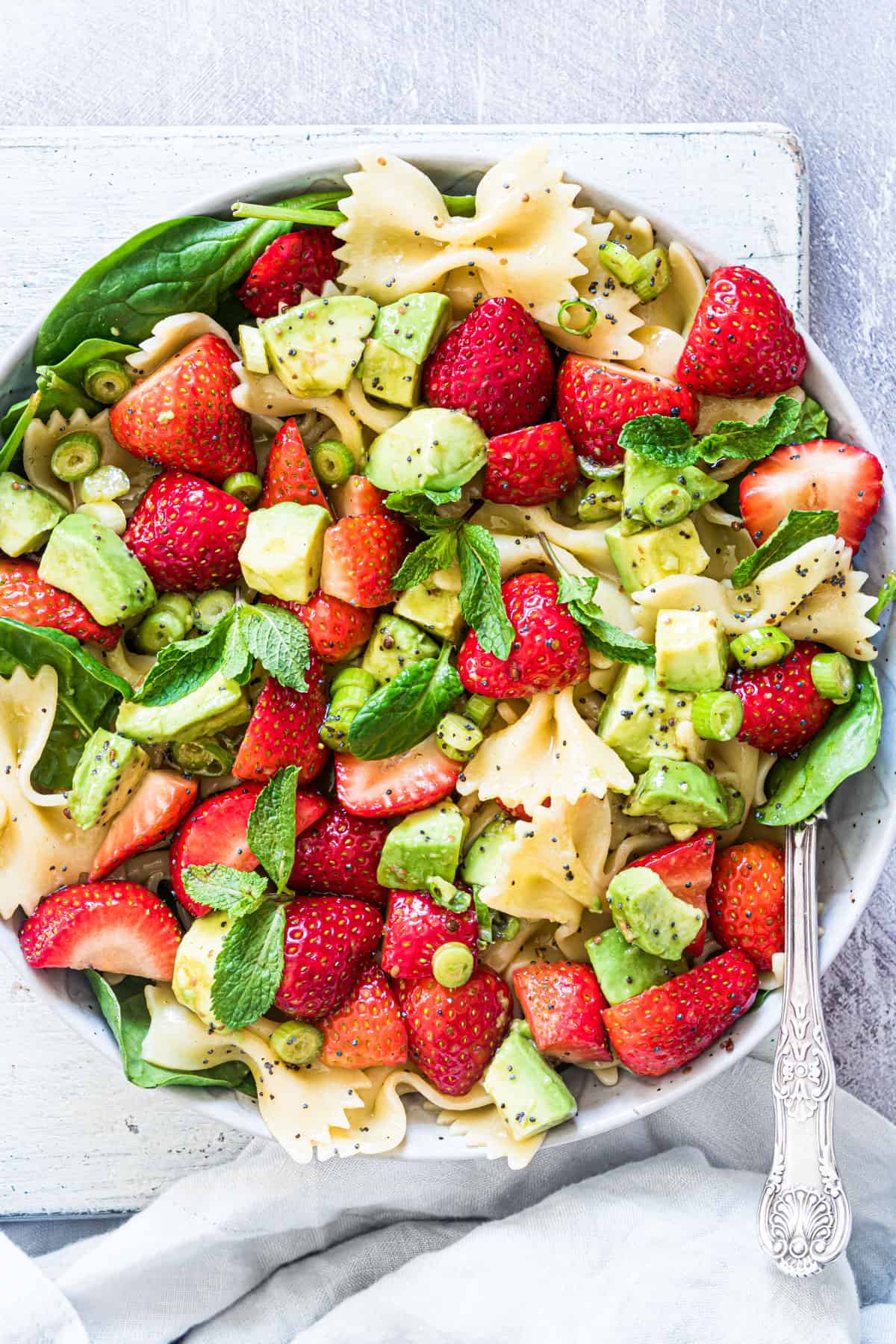 strawberry avocado pasta salad in bowl on counter with spoon and napkin.