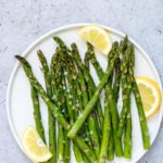 air fryer asparagus served on a white plate with fresh lemon wedges