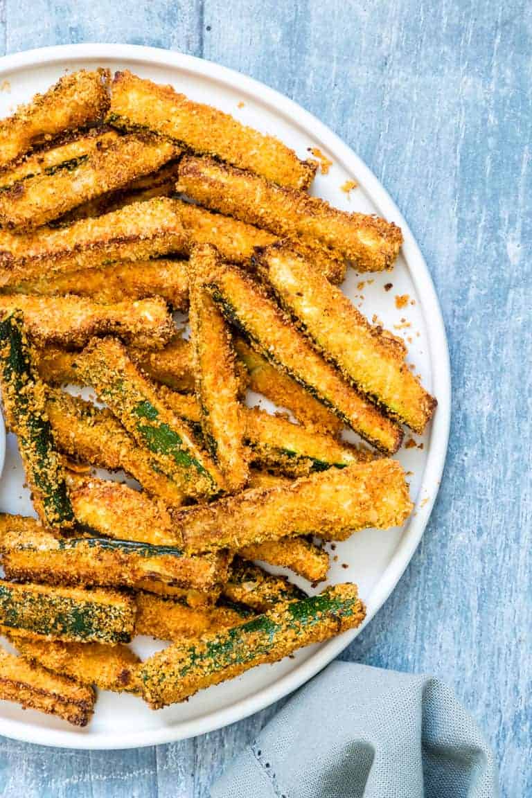 close up of the completed baked zucchini fries on a white plate and ready to serve