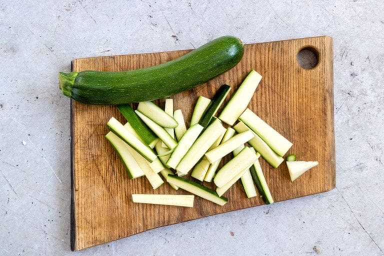 one whole zucchini and one sliced zucchini on a cutting board ready to be made into air fryer zucchini fries