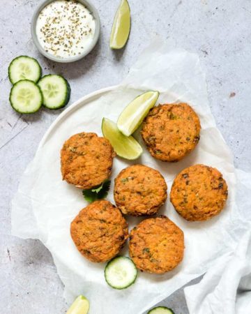 Baked salmon patties served on a white plate with lime wedges, sliced cucumber and homemade dipping sauce
