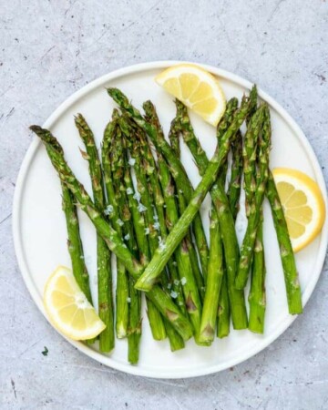 air fryer asparagus served on a white plate with fresh lemon wedges