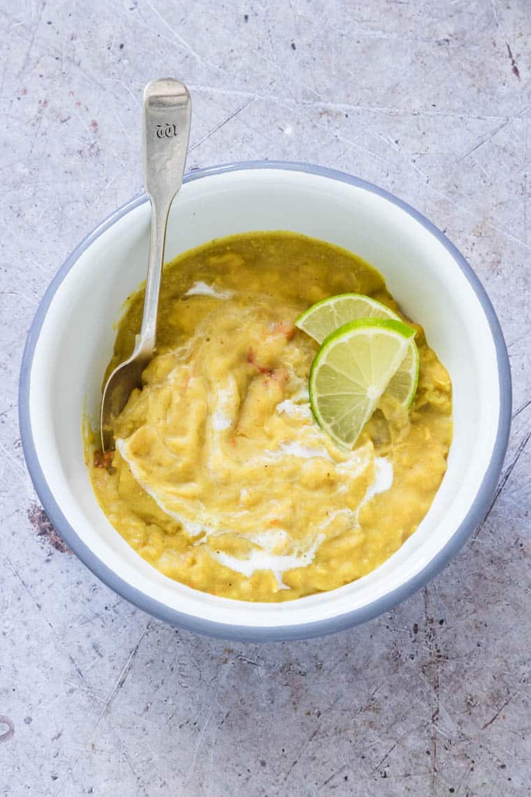 top down view of one bowl filled with instant pot dal and served with a swirl of coconut milk and lime wedges