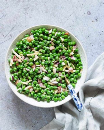 Creamy Pea Salad ready to serve in a white bowl with a blue patterned handled spoon and cloth napkin
