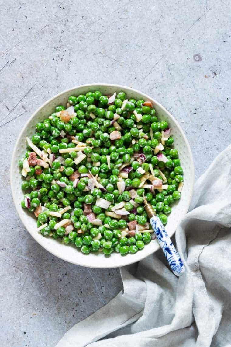 Creamy Pea Salad ready to serve in a white bowl with a blue patterned handled spoon and cloth napkin