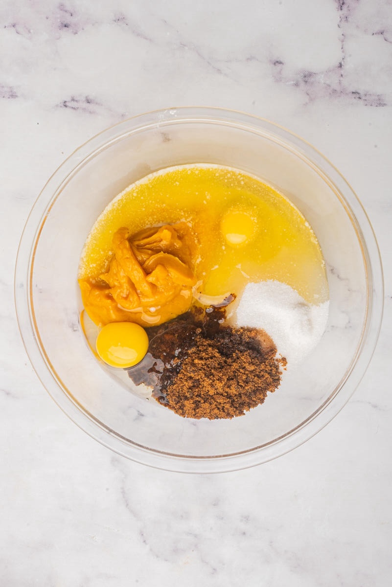 A glass bowl with wet ingredients for baking, including eggs, pumpkin puree, melted butter, brown sugar, and granulated sugar.