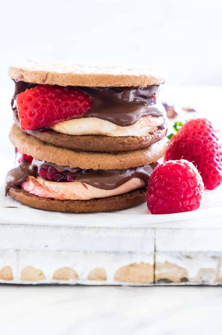 two completed nutella smores stacked and sitting next to two fresh raspberries