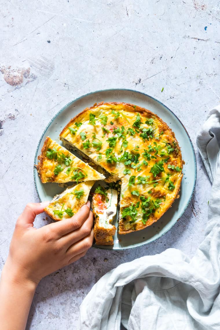 kids hands taking a slice of air fryer breakfast frittata from a plate